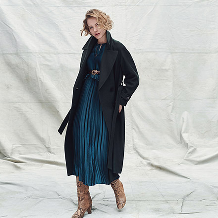 A dark blue teal top over a pleat skirt paired with beige suede boots and a dark coat. Image by Dorothy Perkins.