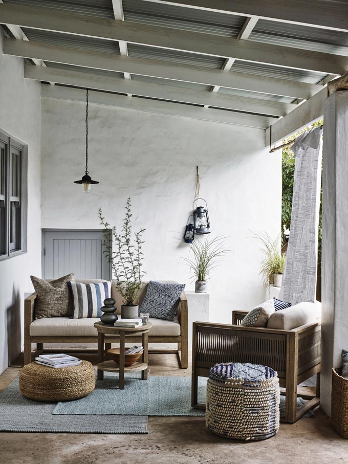 A stylish outdoor space under a rustic pergola, with sofa and armchair and lots of pillows and poufs for sitting comfort. Image via John Lewis.