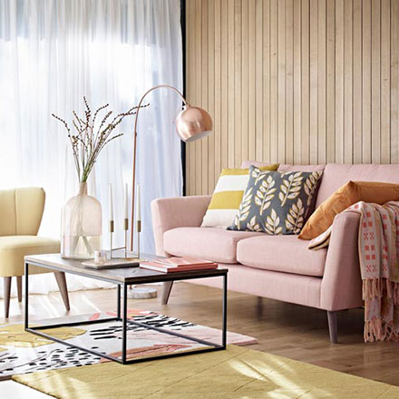 A warm and inviting living room with a soft blush pink sofa, an off white armchair, a coffee table and a wooden accent wall. Image via Marks&Spencer.