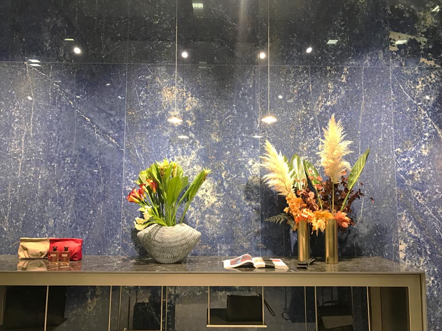 A bathroom installation at Cersaie 2019 from Atlas Concorde using a blue veined marble tile and a black vein marble top console table. 