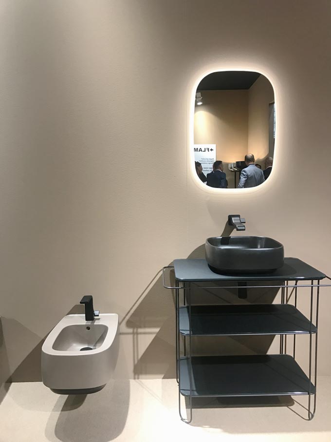 A bathroom installation at the fair of Cersaie 2019 of a beige toilet and a black vanity against a beige wall at the stand of Flaminia.