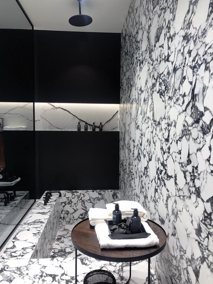 A stunning black and white bathroom with a tub that continues to become an accent wall out of marble tiles.
