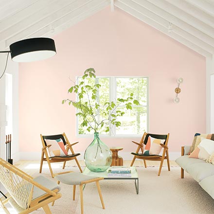 A contemporary and very brights living room with a soft pink wall in the background known as First Light from Benjamin Moore. Image via Benjamin Moore.