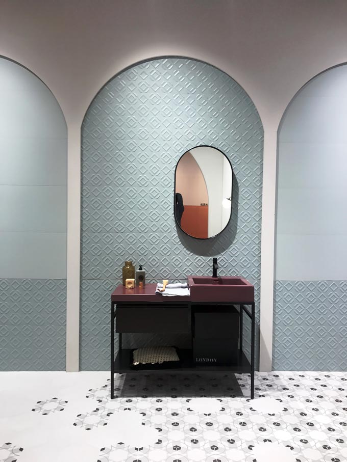 A cyan textured tile on an exhibit booth at Cersaie 2019 with a deep burgundy vanity stand and mirror in front of it. A brilliant setup.