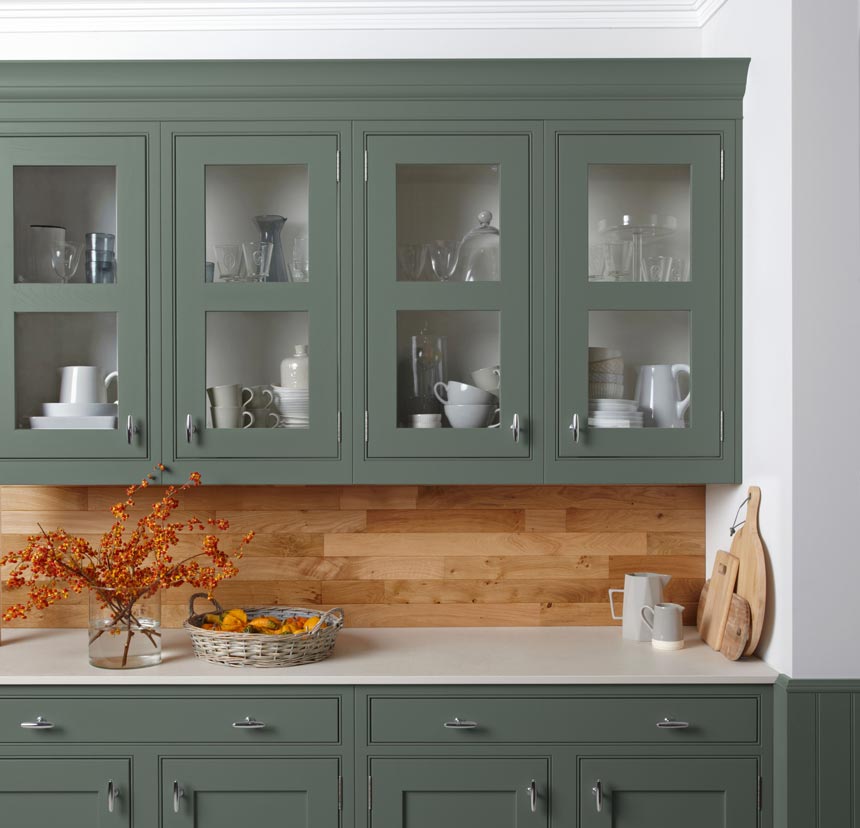 Detail of a beautiful green kitchen cabinetry with a wooden backsplash. Image via Burbidge.