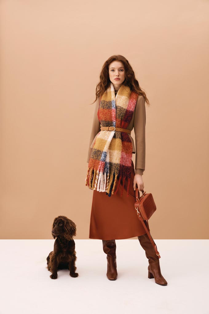 A pasmina worn over a camel coat and a burnt orange skirt and slouchy boots. Note the colors both that cute dog and woman sport so well. Image via Hobbs.