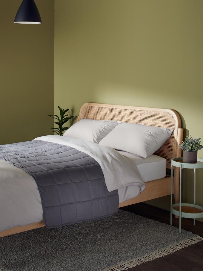 A green bedroom with a beautiful bed that has a cane headboard. Image via John Lewis.