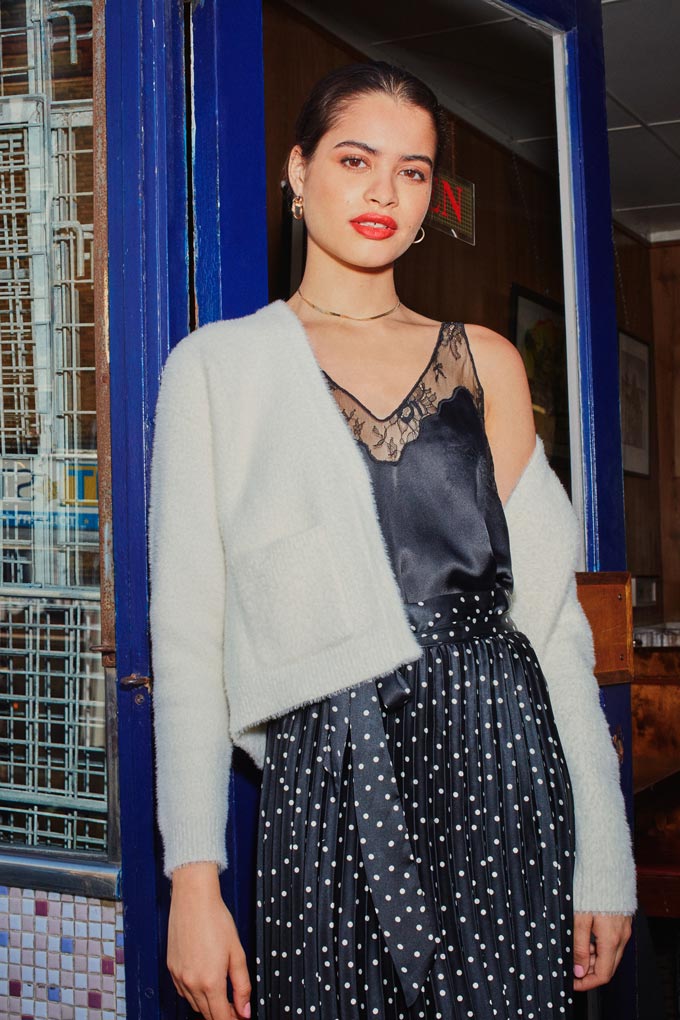 A black cami top paired with a polka dot satin pleat skirt paired with a white jacket. Image via Miss Selfridge.
