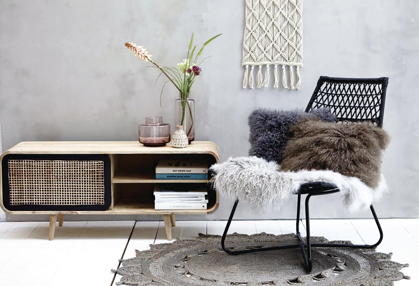 The Lene Bjerre Dea Media Cabinet next to a black rattan chair decorated with soft textiles. Image via Houseology.