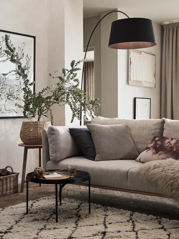 An impossibly chic Scandi-boho living room with an eclectic vibe and a neutral color palette and a few black accents like the floor lamp, the round coffee table and one of the decorative cushions on the sofa. Image by John Lewis.