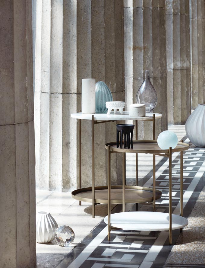 Two Broste Copenhagen Tristan side tables featuring marble and brass placed by some Roman marble columns. Image via Nest.co.uk.