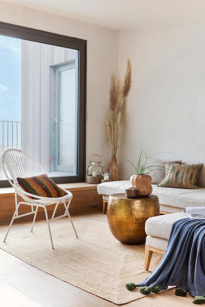 A bright easy going room with a large window, white furnishings, a brass round coffee table. Image via Amara.