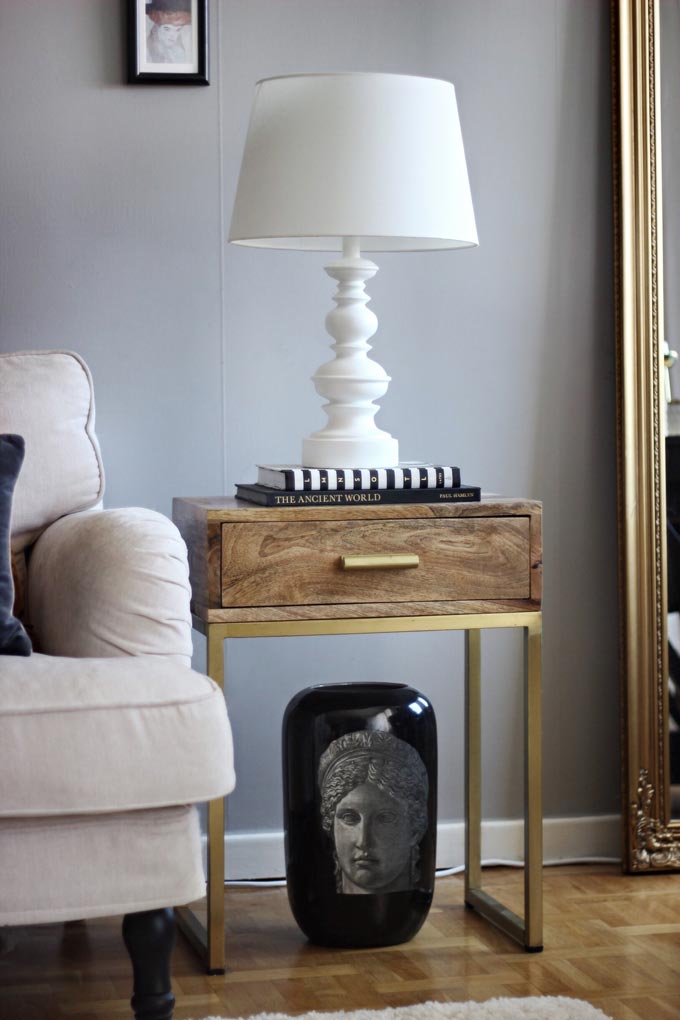 A stylish vignette with an off white sofa, side table with brass details and an all white table lamp resting upon a couple of books laid on the side table. Image via Cult Furniture.