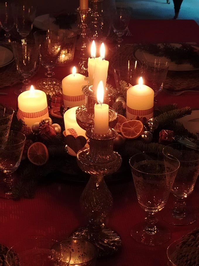 A close up view of an Advent wreath with its burning candles as the centerpiece on a Christmas table setting.