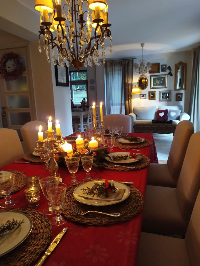 A beautifully styled dining table for Christmas with a red tablecloth and an Advent wreath. In the background there's a sofa with an art gallery wall.