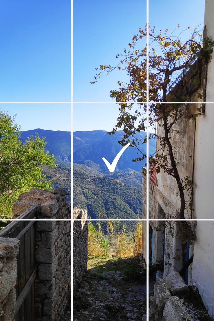 Looking from a passage at the blue green mountains in the background. Picture taken at Arachova, a villiage in Greece. A grid like overlay with a check mark in the middle pinpoints the center of the image.