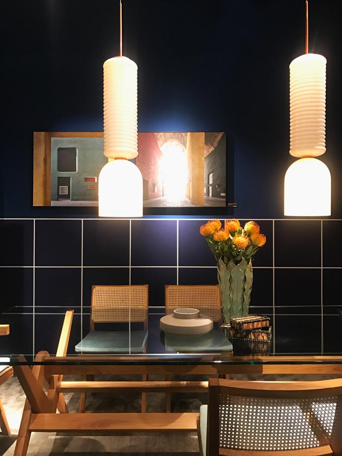A dining set against a dark blue tiled wall with two pendant lights as seen at Cassina.