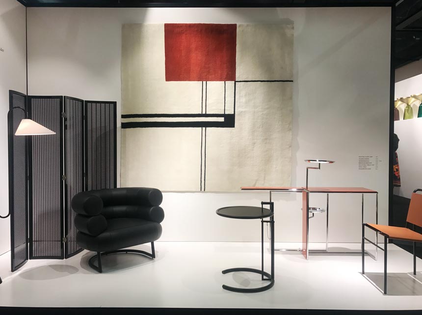 A booth at the imm Cologne 2020. A black divider, armchair, a wall tapestry and tables all part of this installation at Classicon.