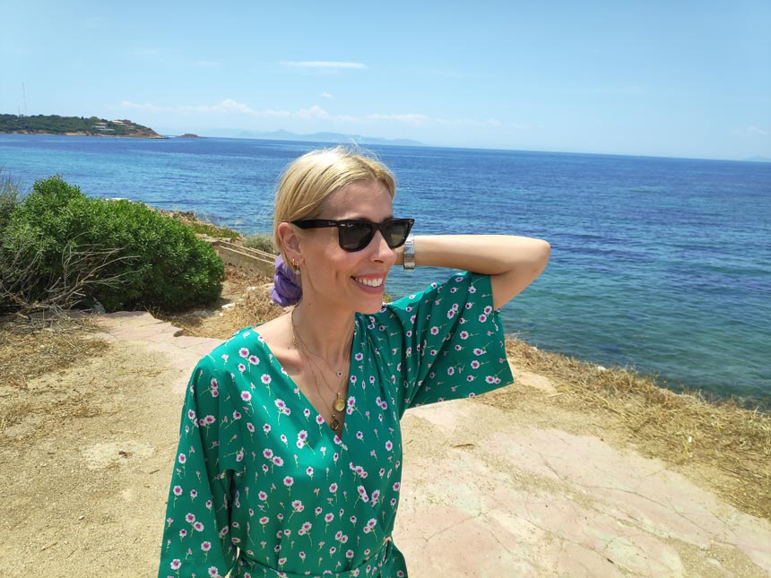 Elisabeth in a green playsuit near a coastline wearing shades.
