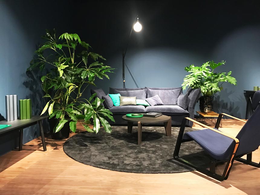 A dark grey contemporary sitting lounge by Vitra that includes a sofa, an armchair and some big plants.
