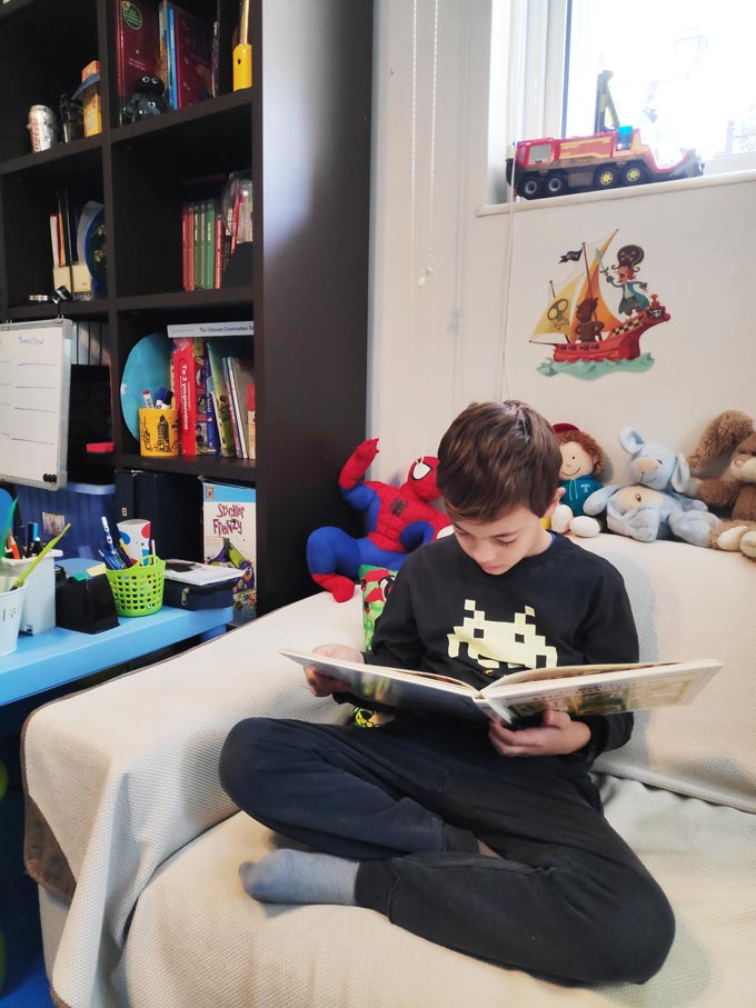 Tips for encouraging kids reading: A boy sitting on a sofa besides a bookcase reading a book. Image by Velvet.