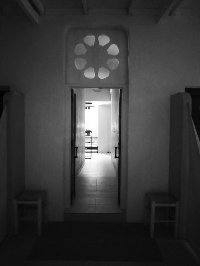 A black and white image of an open entry door lending views to a corridor and a room inside.