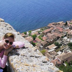 Velvet, the author, by the wall of a Medieval fortress in Monemvasia. In the background, the castle town of Monemvasia and the Aegean Sea.