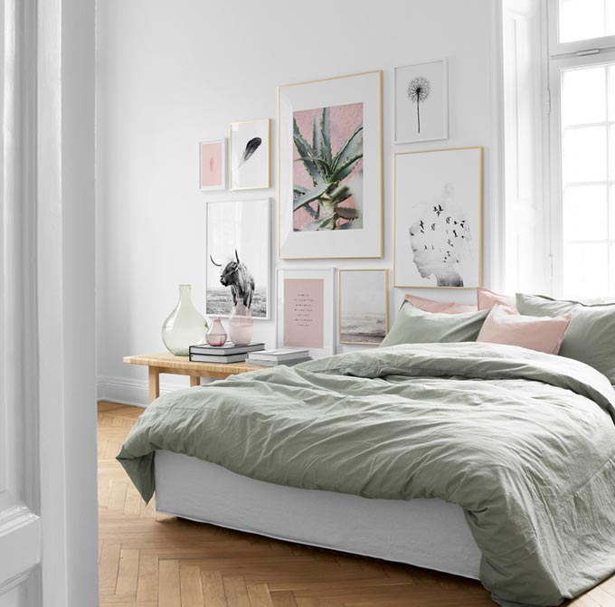 A contemporary bright white bedroom with soft sage and pink accents, a bench for a bedside table and a gorgeous art gallery wall. Image: Desenio.