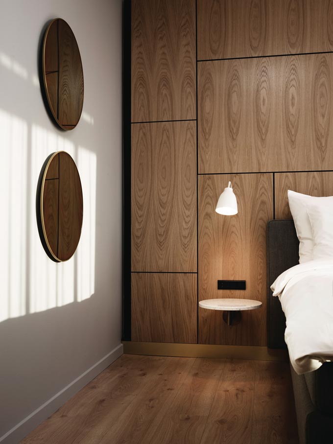 The Fritz Hansen Caravaggio Read Wall Light standing out against the wooden wall paneling, casting light upon a small white shelf that serves as a nightstand. Very sophisticated. Image: Nest.co.uk.