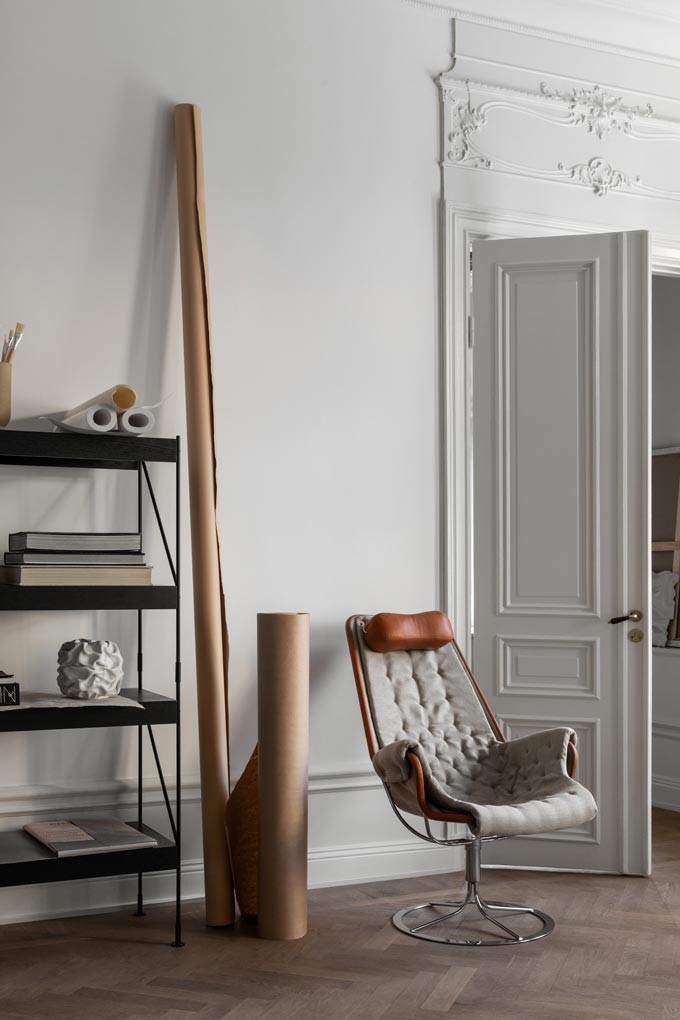 A rack of black shelves with an accent lounge chair besides it. Image by Monica Steffensen for Menu.