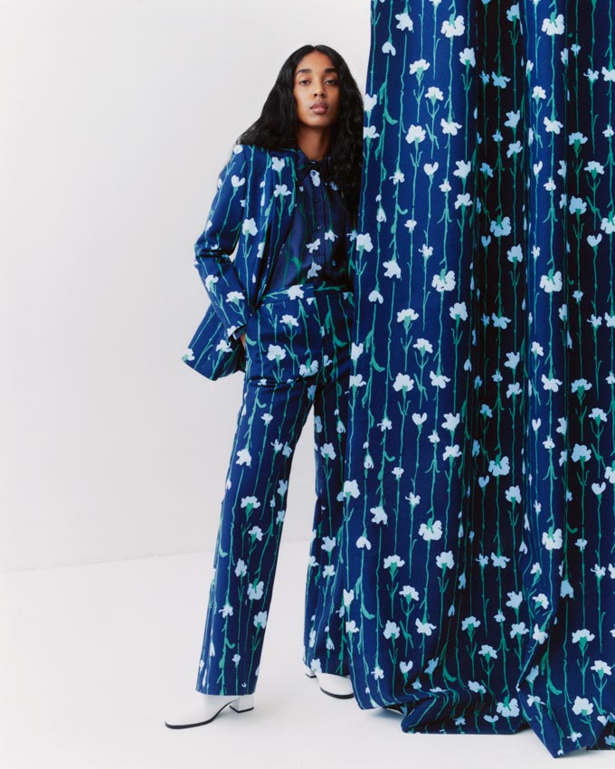 A woman dressed in a classic blue suit with a white flower print, standing next to a matching curtain. Image: Marimekko.