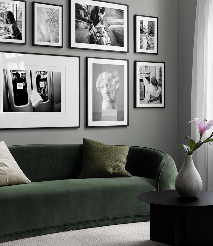 A moody living room with a fir green velvet sofa, featuring a black and white photography print gallery wall. Image: Desenio.