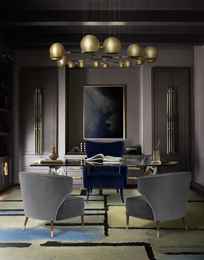 Decorating with intention. A dark and moody but very chic home office with a large golden finish chandelier and a glass top desk. Image: Brabbu Design Forces.