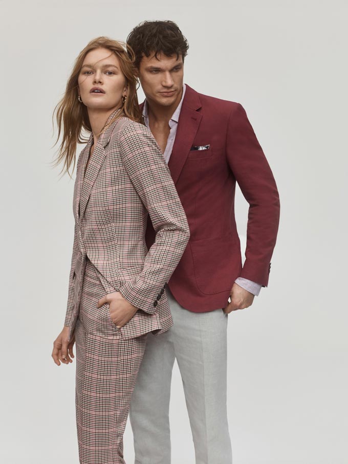 A couple. Woman in a check suit and man in light grey pants paired with a muted burgundy suit jacket. Image: SABA.