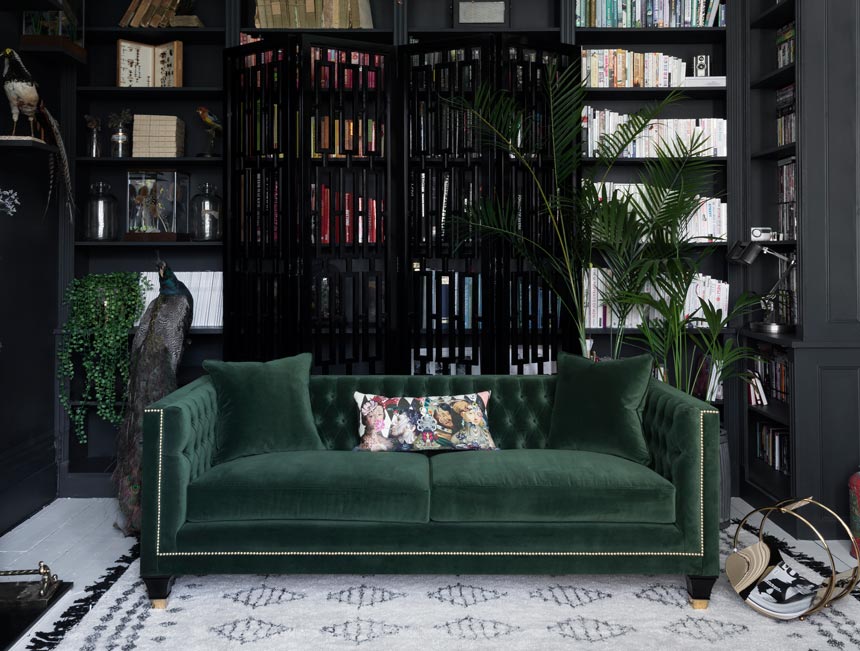 A stunning green velvet sofa from the Balfour designer sofa collection in front of a black screen and a wall to wall black bookcase. Image: Sweetpea & Willow.