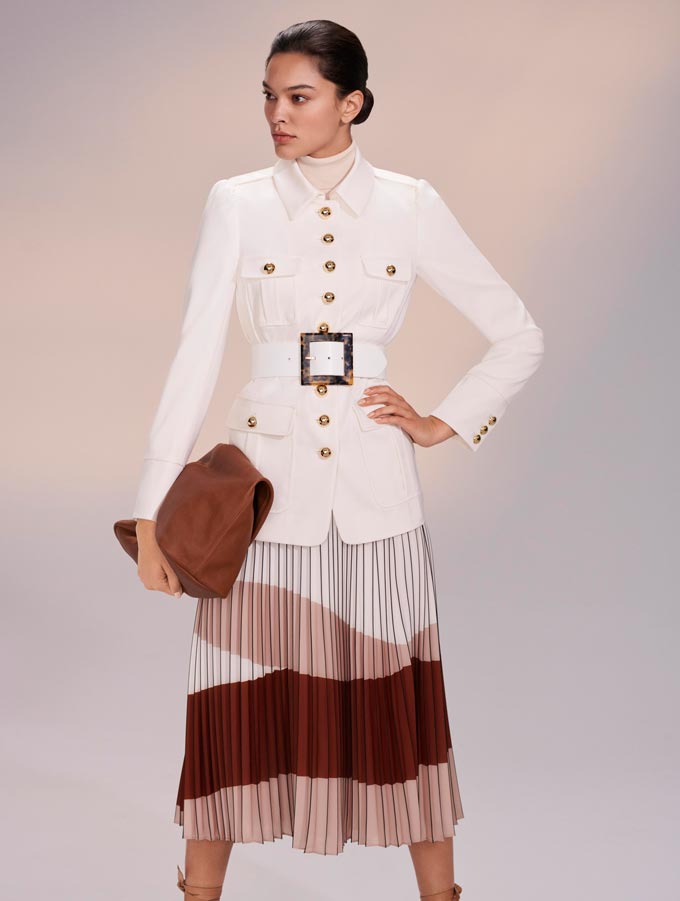 Transitional winter to spring outfits. A chic woman dressed in a white utilitarian jacket paired with a color blocked skirt in earthy tones. Image: Hobbs.