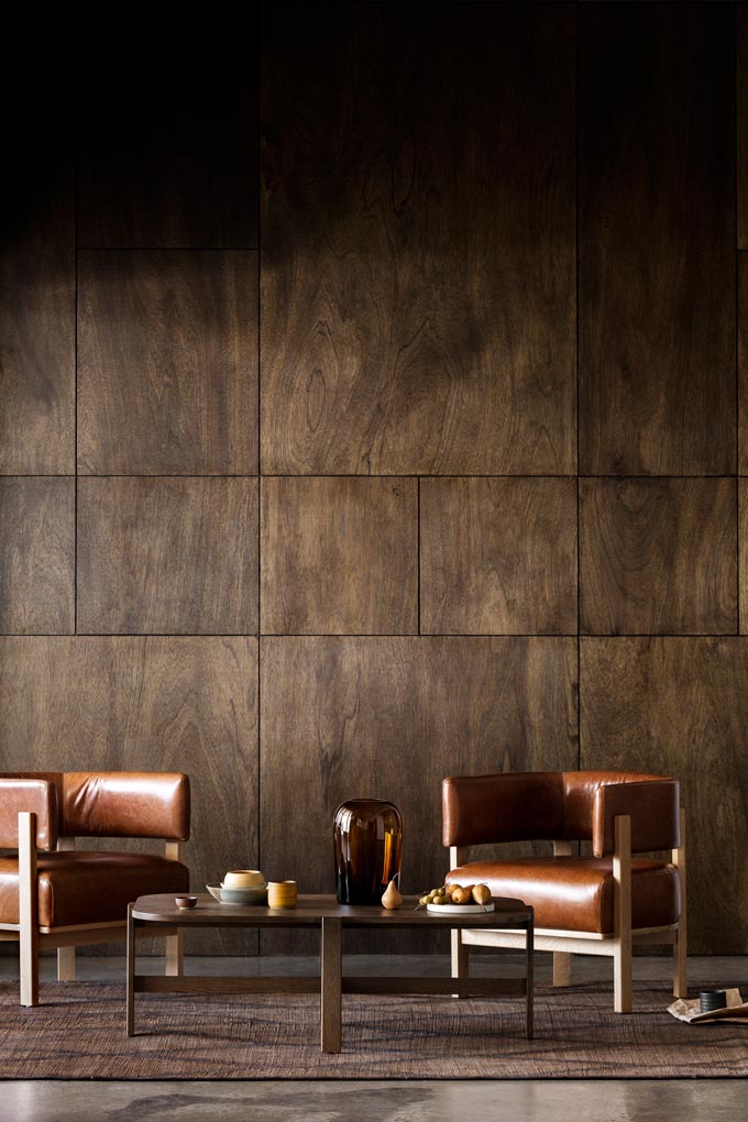 A dark and moody earth toned living set with a brown cladding accent wall, two gorgeous leather armchairs and a round coffee table. Image: Martina Gemmola for Anaca Studio.