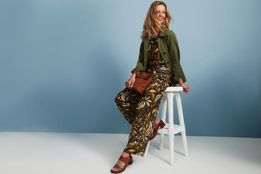 A khaki jumpsuit with a big flower print paired with a tan leather bag and sandals and a khaki jacket. Image: Matalan.