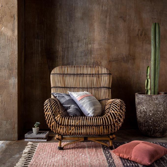 An earth toned wall acting as the backdrop to a rattan armchair. Image: KAS Australia
