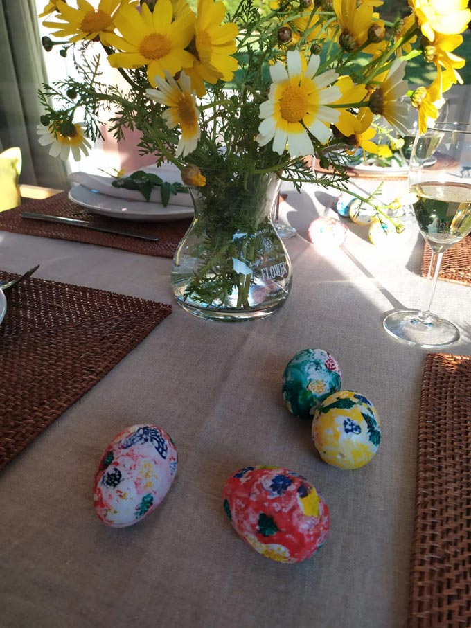 Hand painted eggs and a vase with yellow daisies on a dining table.