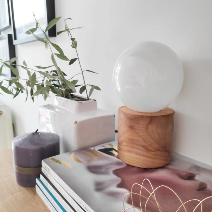 A stack of magazines next to a white vase and a muted purple candle on a dresser.