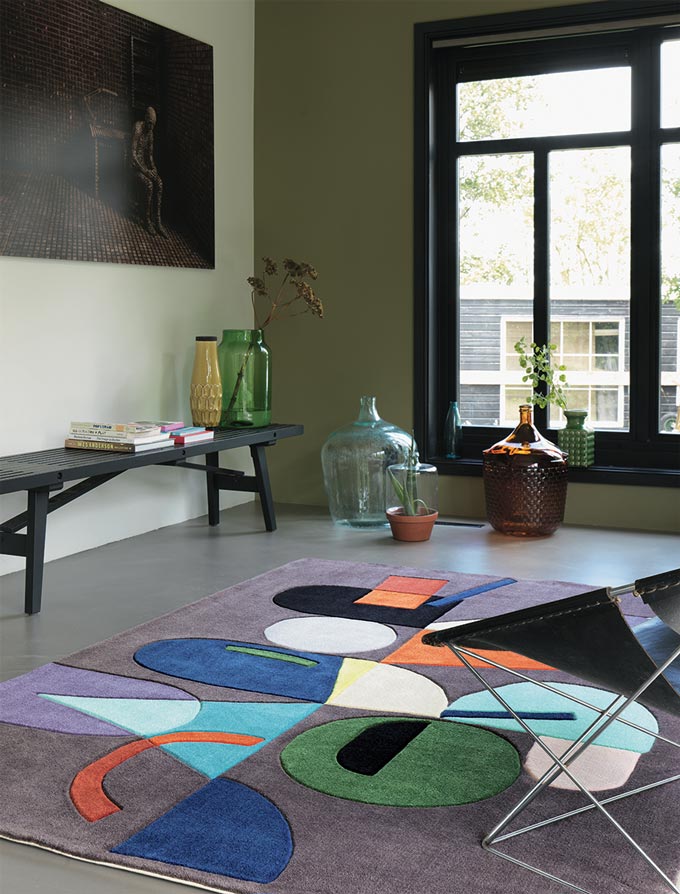 A contemporary space with a big window, a bench with decor on it and an armchair resting upon a Bauhaus-inspired design area rug. Via Traumteppich.com.