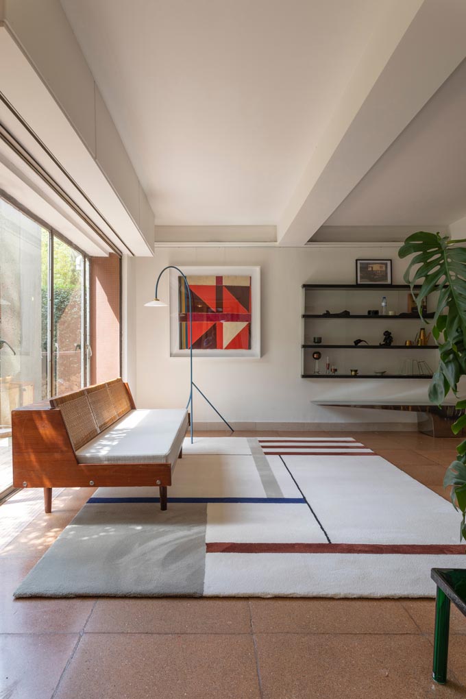 A contemporary living room with minimal decor and a strong Bauhaus feel due to its sofa, block pattern artwork on the wall and area rug on the floor.