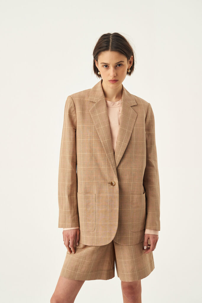 A woman wearing a check suit jacket and coordinating check shorts. Via Oroton.