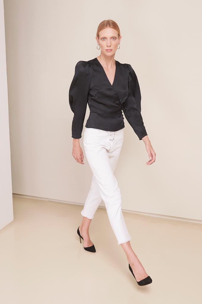 A stylish woman dressed in a black satin shirt with puffed sleeves, white denim pants and black heels. Via Magali Pascal.