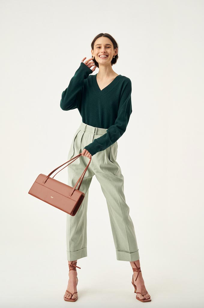 A stylish woman wearing a green V neck sweater paired with a mint green pair of pants. Via Oroton.