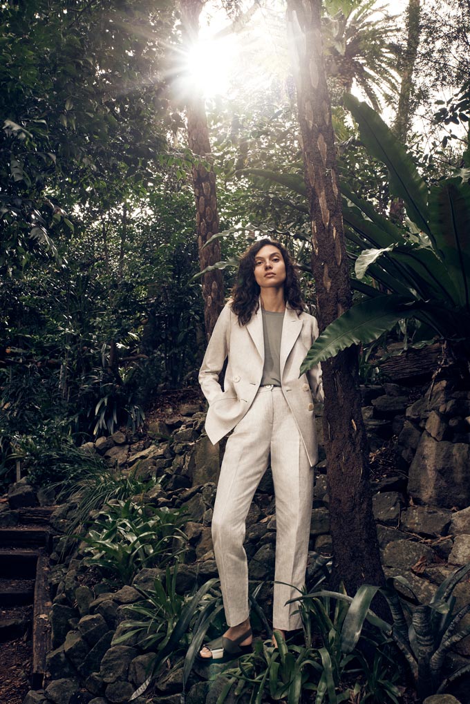 A woman in a greenery nature setting dressed in an off white power suit. Via Sportscraft.