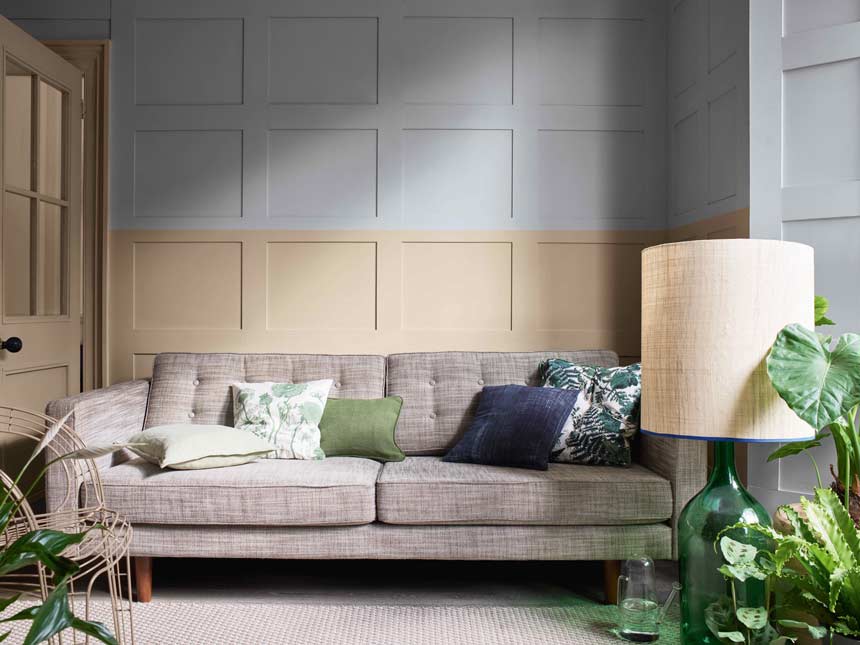 A living room with a beige sofa against a color blocked panelled wall in Brave Ground and grey. Via Dulux.