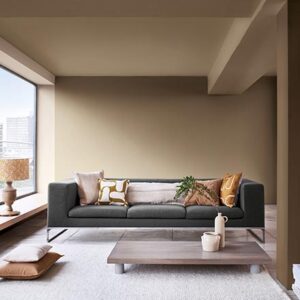 A contemporary living space with large windows, a dark grey sofa, a low coffee table and walls in Dulux Brave Ground beige. Via Dulux.
