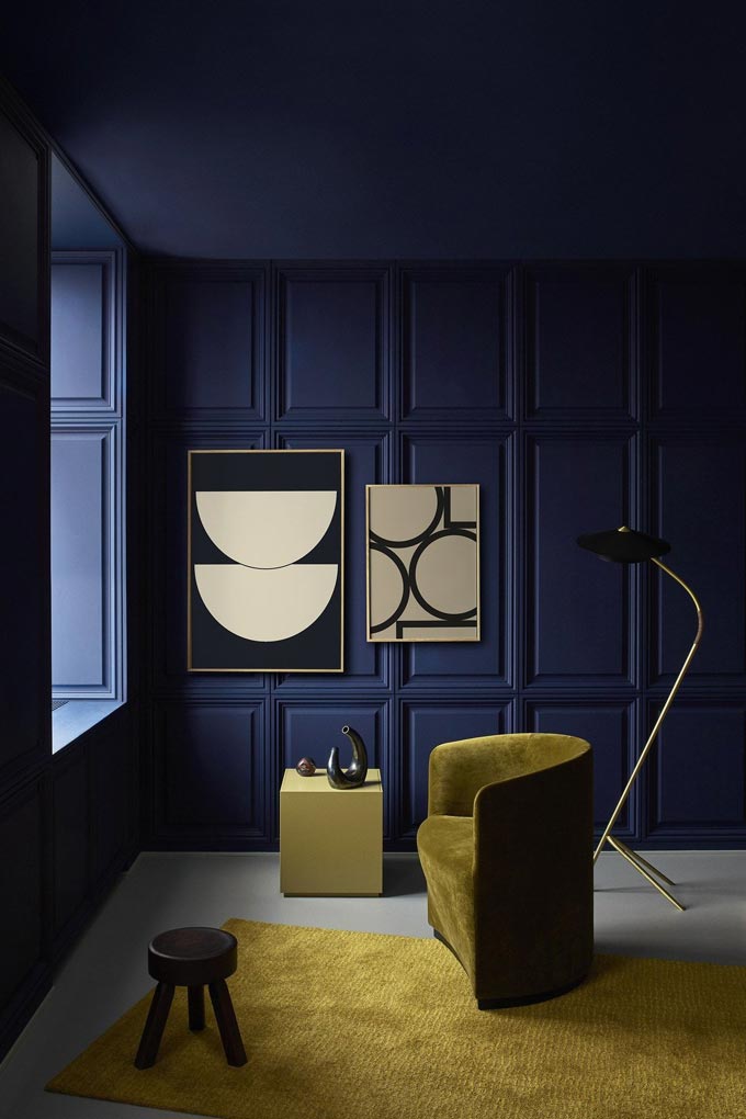 An all navy blue room featuring on olive khaki velvet armchair, an area rug and two Bauhaus inspired art prints on the wall. Via Nest.co.uk.